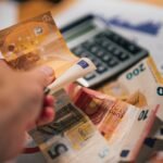 A person putting money into a calculator